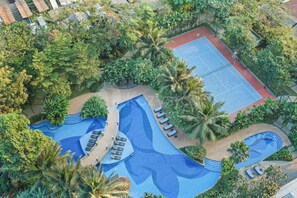 Eine Luftaufnahme eines Resorts mit Swimmingpool, Liegestühlen und Tennisplatz, umgeben von üppiger Vegetation.
