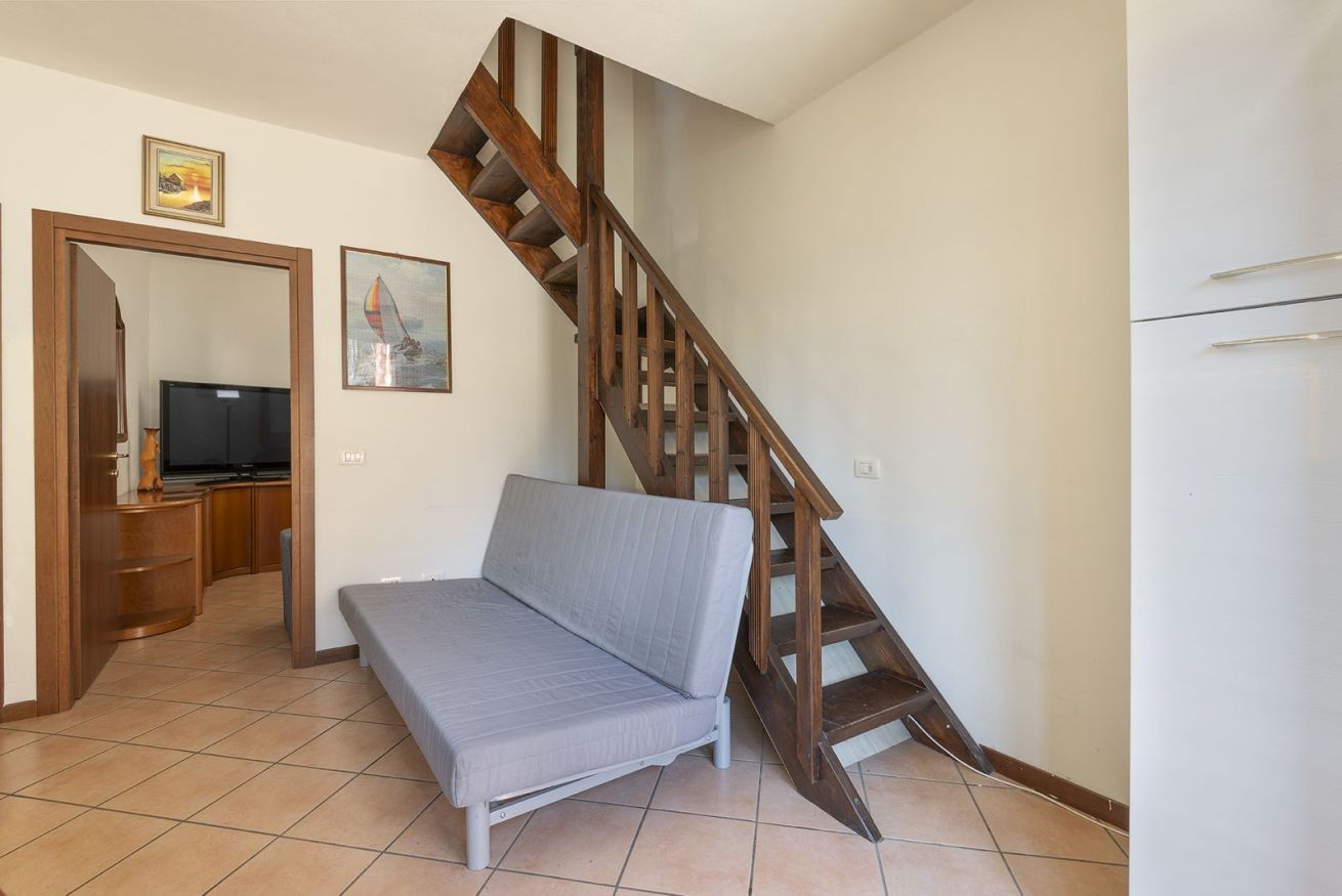 A room with a sofa, a wooden staircase, a television, and a painting on the wall.
