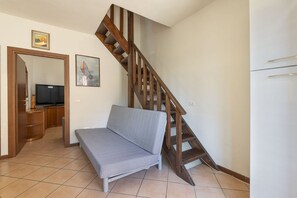 A room with a sofa, a wooden staircase, a television, and a painting on the wall.