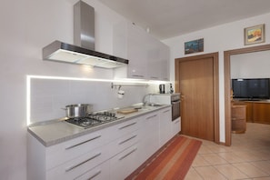 A modern kitchen with white cabinets, a stainless steel range hood, a gas stove, and a built-in oven.
