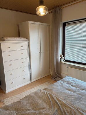 Ein Schlafzimmer mit einem Bett, einem Kleiderschrank, einer Heizung und einem Fenster mit Jalousien.