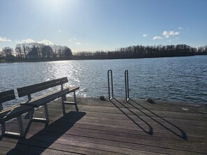 Eine Holzstege mit einer Bank und Metallgeländern, der in einen ruhigen See führt.