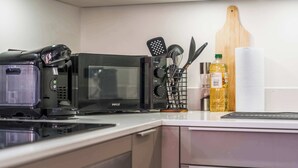 A kitchen with a microwave, a spice rack, a bottle of oil, and a wooden cutting board. - Modern Flat In Jewellery Quarter, Free Parking (Birmingham)