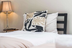 A bed with white bedding, a black and beige pillow, and a bedside table with a lamp. - Modern Flat In Jewellery Quarter, Free Parking (Birmingham)