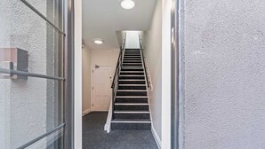 A narrow hallway leading to a staircase with a handrail, a door at the end, and a textured wall on one side. - Modern Flat In Jewellery Quarter, Free Parking (Birmingham)