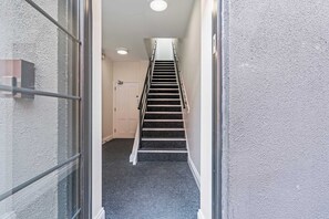 Ein schmaler Flur, der zu einer Treppe mit Handlauf und einer Tür am Ende führt, mit einer strukturierten Wand an einer Seite.