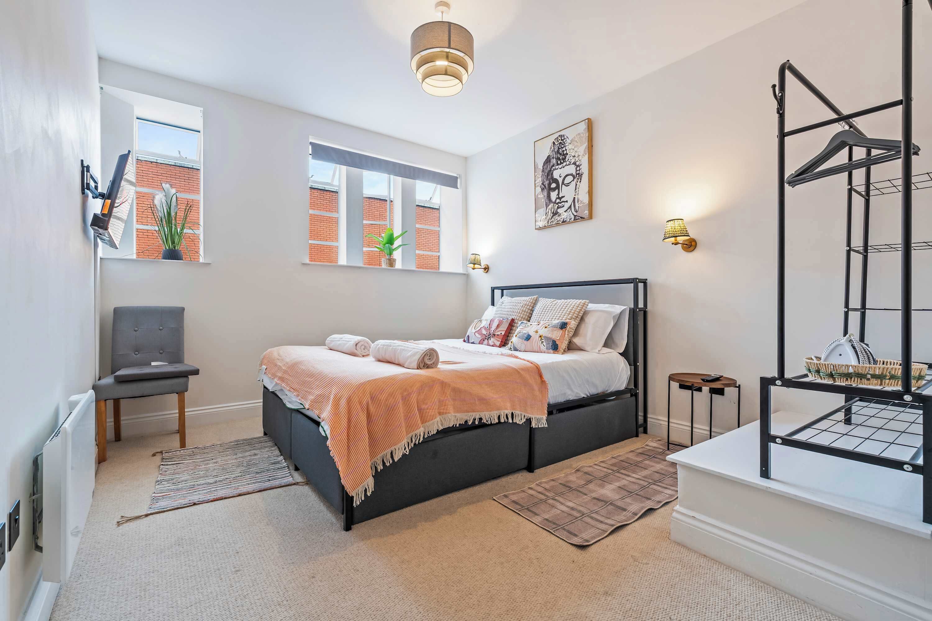 A modern bedroom with a bed, a chair, a radiator, a window, and a wall-mounted shelf.