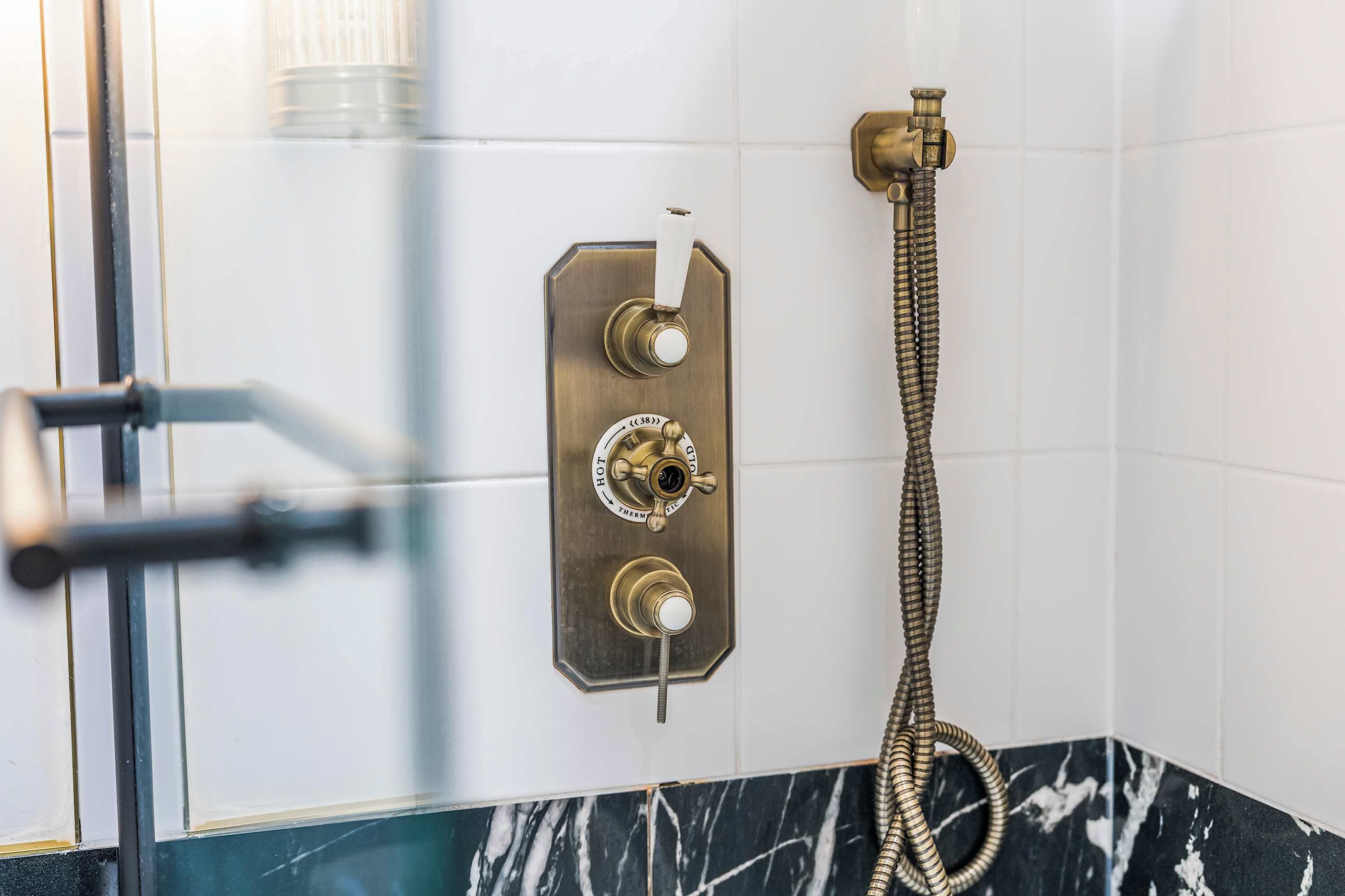 A bathroom with a shower control panel, a handheld showerhead, and a glass door.