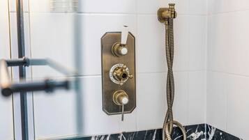 A bathroom with a shower control panel, a handheld showerhead, and a glass door.