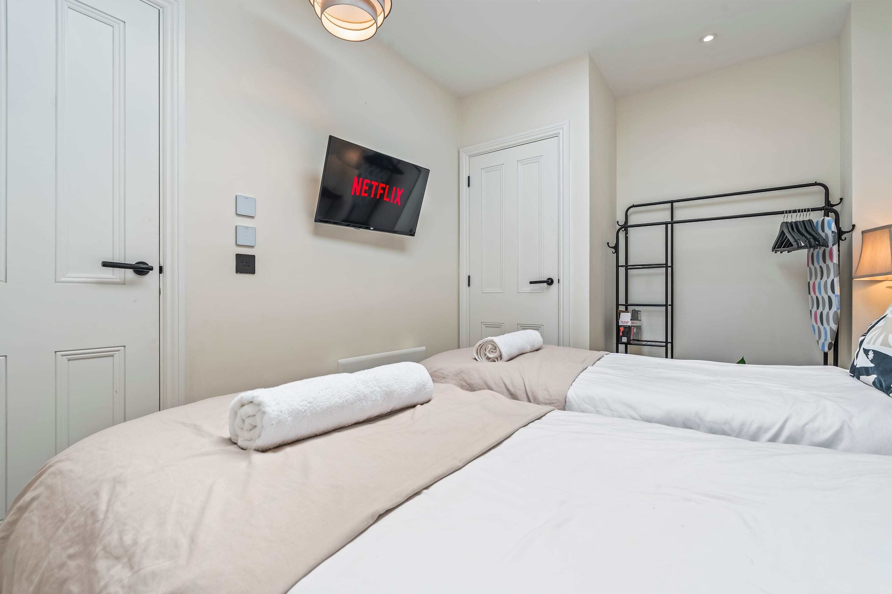 A hotel room with two beds, a TV mounted on the wall, and a clothing rack.