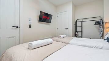 A hotel room with two beds, a TV mounted on the wall, and a clothing rack.