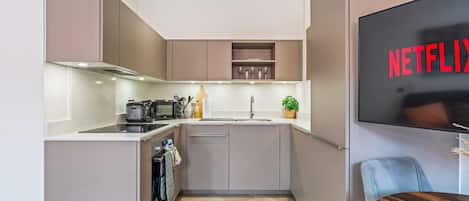 A modern kitchen with a built-in microwave, toaster, and sink. There is a small plant on the counter and a wall-mounted TV displaying the Netflix logo.