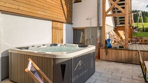 A hot tub outside a building with a wooden deck and a swing set. - Grand Chalet Hochfilzen (Hochfilzen)