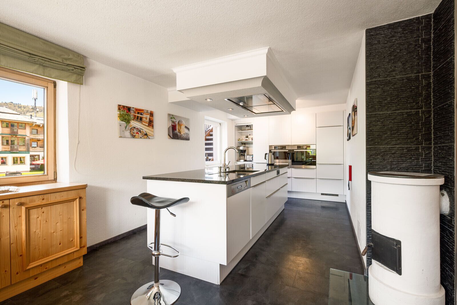 Een moderne keuken met een centraal eiland, witte kasten en uitzicht op een woongebied.