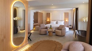 Una habitación de hotel moderna con una cama grande, dos sillones, una mesa de centro y un espejo.