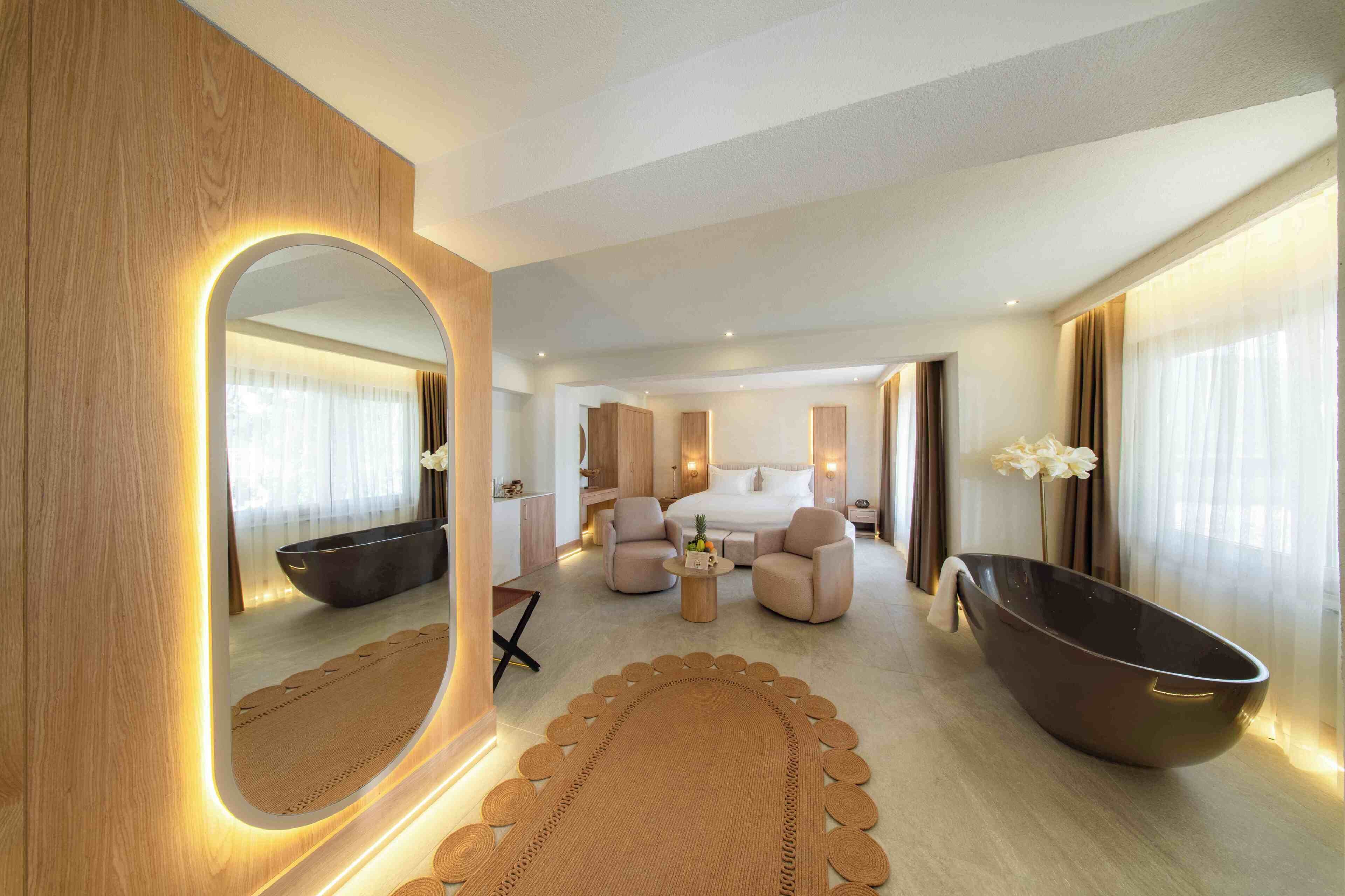 Una habitación de hotel moderna con un espejo grande, una bañera, un sofá, una mesita de café y una cama.