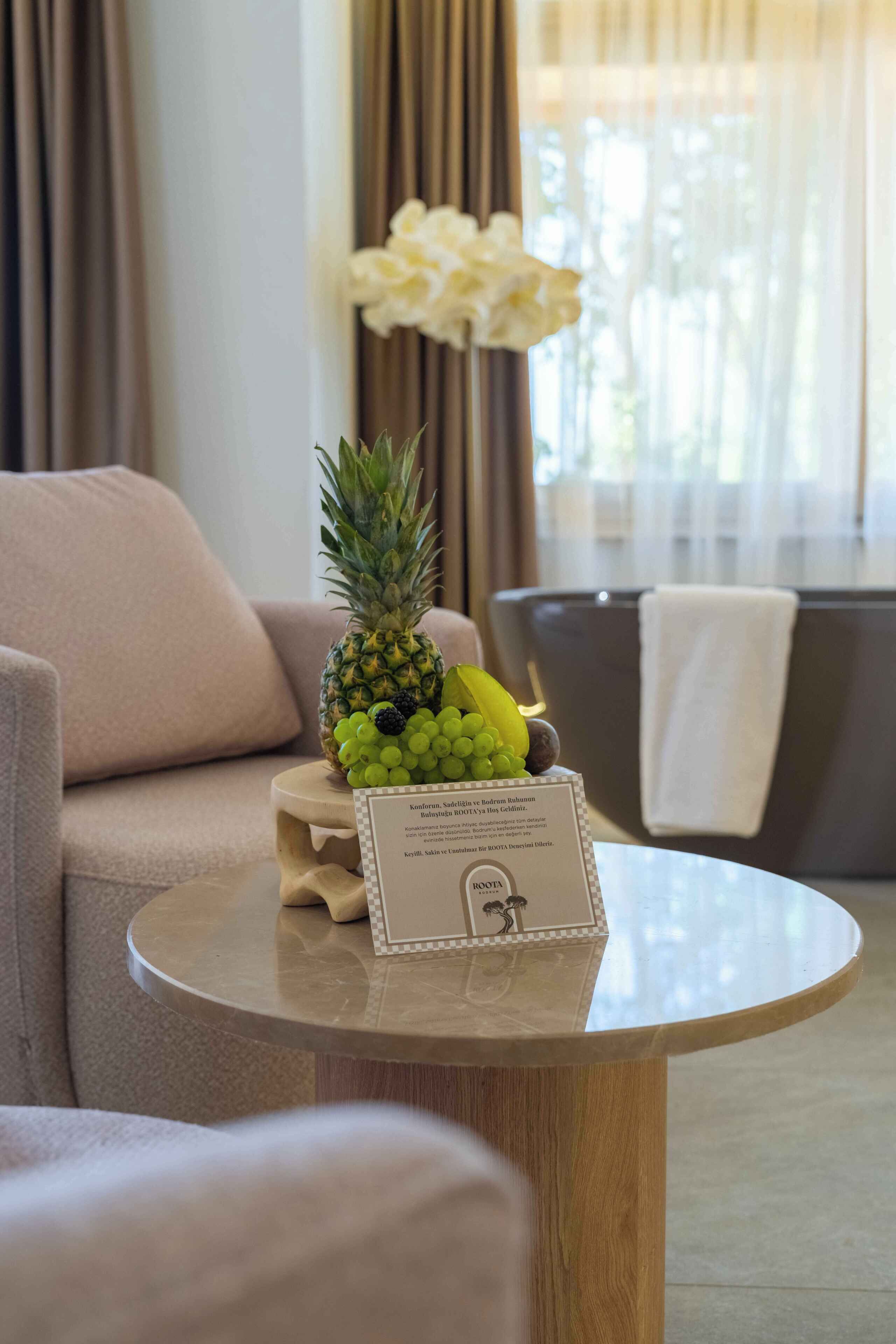 Ein Hotelzimmer mit einem runden Tisch, einer Ananas mit Trauben und einem Schild mit Text.