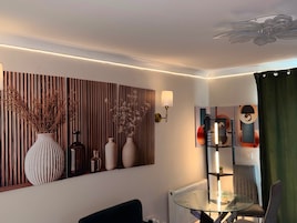 Un salón moderno con una mesa de centro de vidrio, un sofá negro, un radiador y una estantería con adornos.