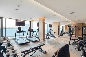 Un gimnasio moderno con cintas de correr, mancuernas y equipo de ejercicio, ventanas amplias y vistas al agua.