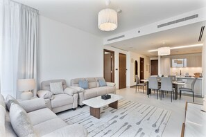 A modern living room with a sofa set, a coffee table, and a dining area with chairs and a table. - 2BR Apartment With iconic view+Ample of amenities (Dubai)