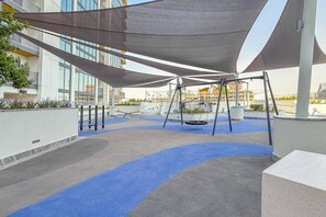 An outdoor area with a swing set, a shaded seating area, and a blue pathway. - 2BR Apartment With iconic view+Ample of amenities (Dubai)
