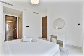 A modern hotel room with a large bed, a round mirror, a small fireplace, and a walk-in closet. - 2BR Apartment With iconic view+Ample of amenities (Dubai)