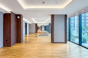 Een moderne hotelgang met houten vloeren, grote ramen en uitzicht op de stad.