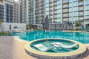 A modern hotel with a large outdoor swimming pool, lounge chairs, and a circular hot tub area. - 2BR Apartment With iconic view+Ample of amenities (Dubai)