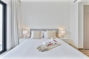 Hotelkamer met een groot bed, twee bedlampen, een raam met gordijnen en een handdoek met het logo van het hotel.