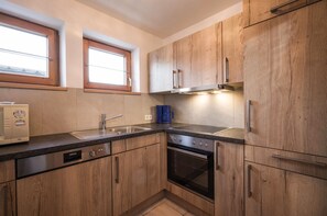 A kitchen with wooden cabinets, a built-in oven, a dishwasher, and a window above the sink. - Haus Adler 2 by Alpine Host Helpers (Westendorf)