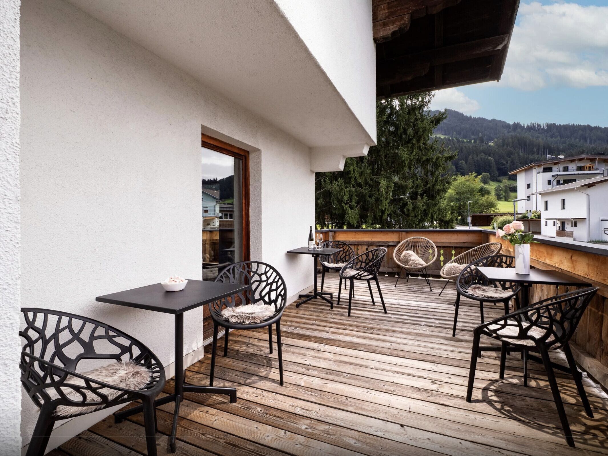 A wooden deck with outdoor seating, including tables and chairs, overlooking a mountainous landscape.