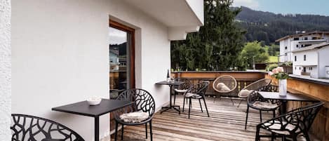 A wooden deck with outdoor seating, including tables and chairs, overlooking a mountainous landscape.