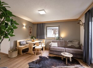 A cozy living room with a wooden bench, a sofa, a coffee table, and a dining table. - Haus Adler 2 by Alpine Host Helpers (Westendorf)