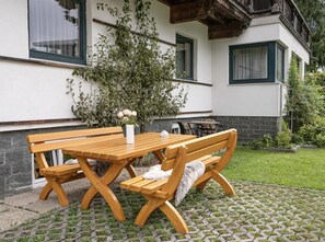 A wooden bench and table set on a paved area with a white building in the background. - Haus Adler 3 by Alpine Host Helpers (Westendorf)