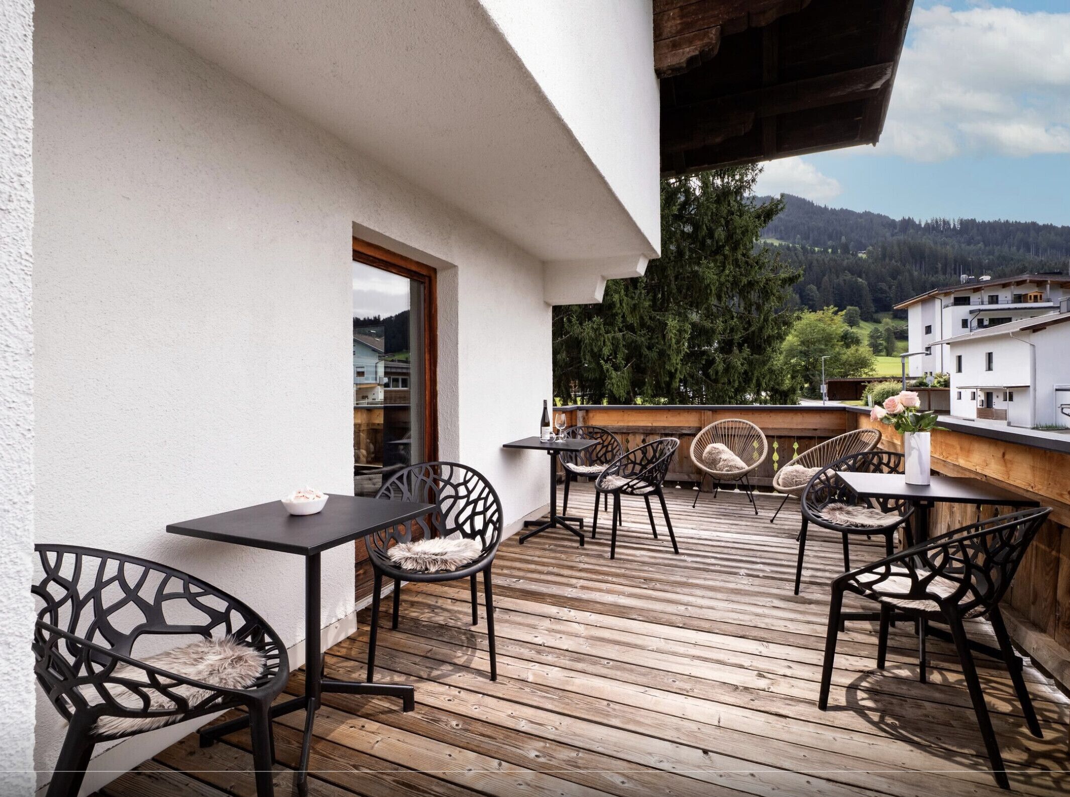 Une terrasse extérieure avec un plancher en bois, des chaises en métal noir et une table.