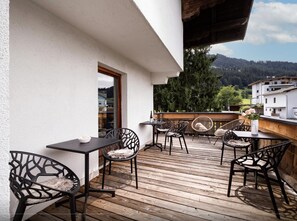 Eine Terrasse im Freien mit Holzboden, schwarzen Metallstühlen und einem Tisch.