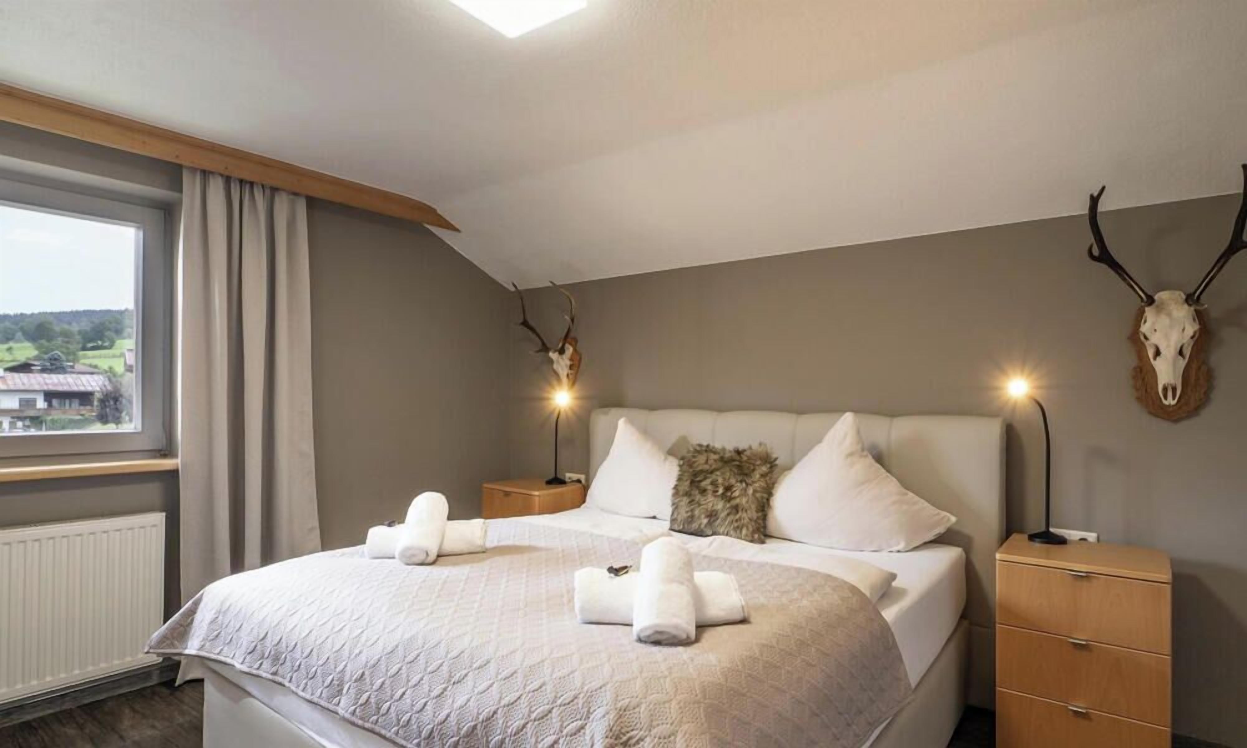 Une chambre à coucher avec un lit, deux tables de chevet, une fenêtre avec des rideaux et une vue sur l’extérieur.