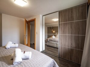 A bedroom with a large bed, a wooden wardrobe, and a mirror reflecting a bathroom with a bed and a deer head decoration. - Haus Adler 4 by Alpine Host Helpers (Westendorf)