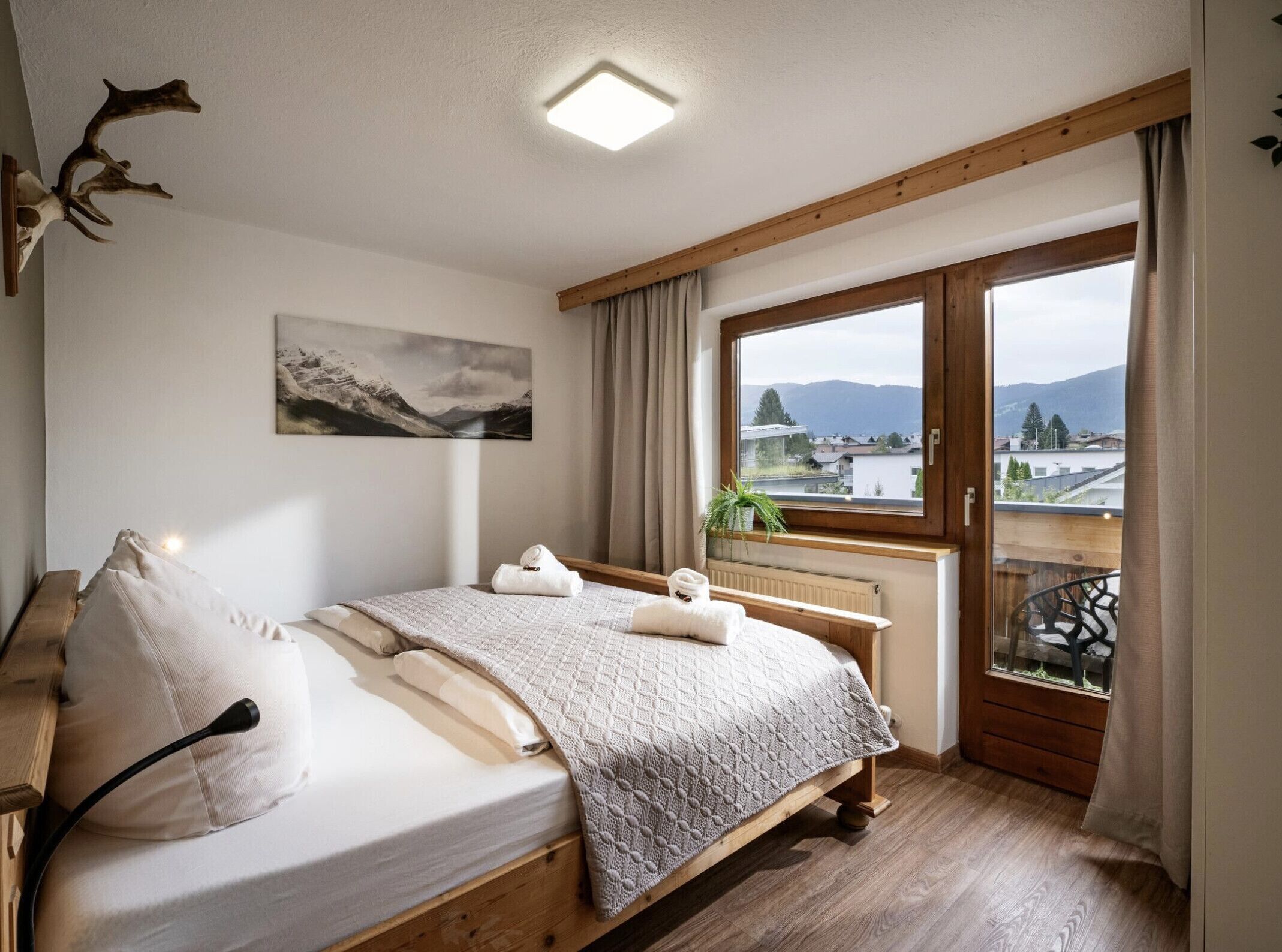 Un dormitorio con cama, ventana con vistas, un cuadro en la pared y una lámpara en el techo.
