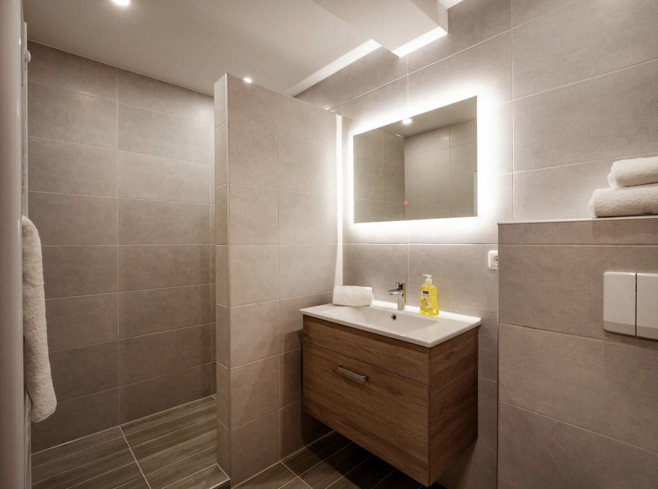 A modern bathroom with a walk-in shower, a wooden vanity with a mirror, and a towel rack.