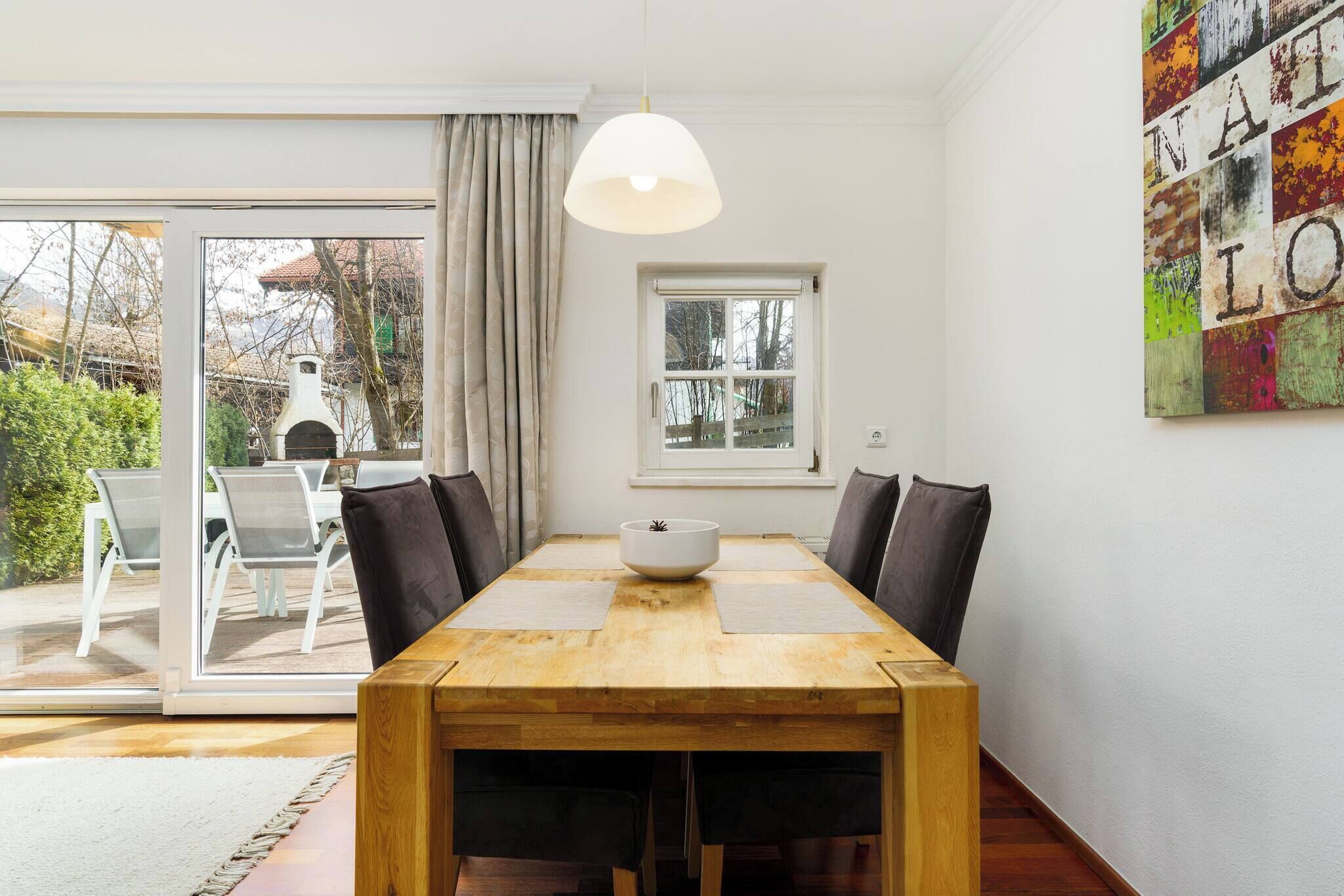 Een eetgedeelte met een houten tafel, stoelen, een witte schaal en een hanglamp.
