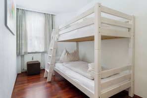 Ein Etagenbett in einem Zimmer mit Fenster, Heizkörper und Holzboden, erreichbar über eine Klapptreppe.