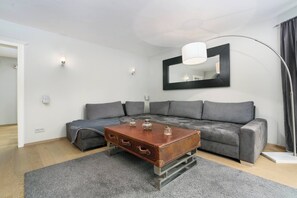 Ein modernes Wohnzimmer mit grauem Sofa, einem Holztisch und einem großen Spiegel an der Wand.