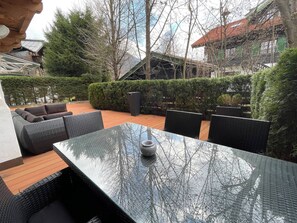 Ein Terrassenbereich mit Tischplatte aus Glas, Korbmöbeln und einem Blumentopf.