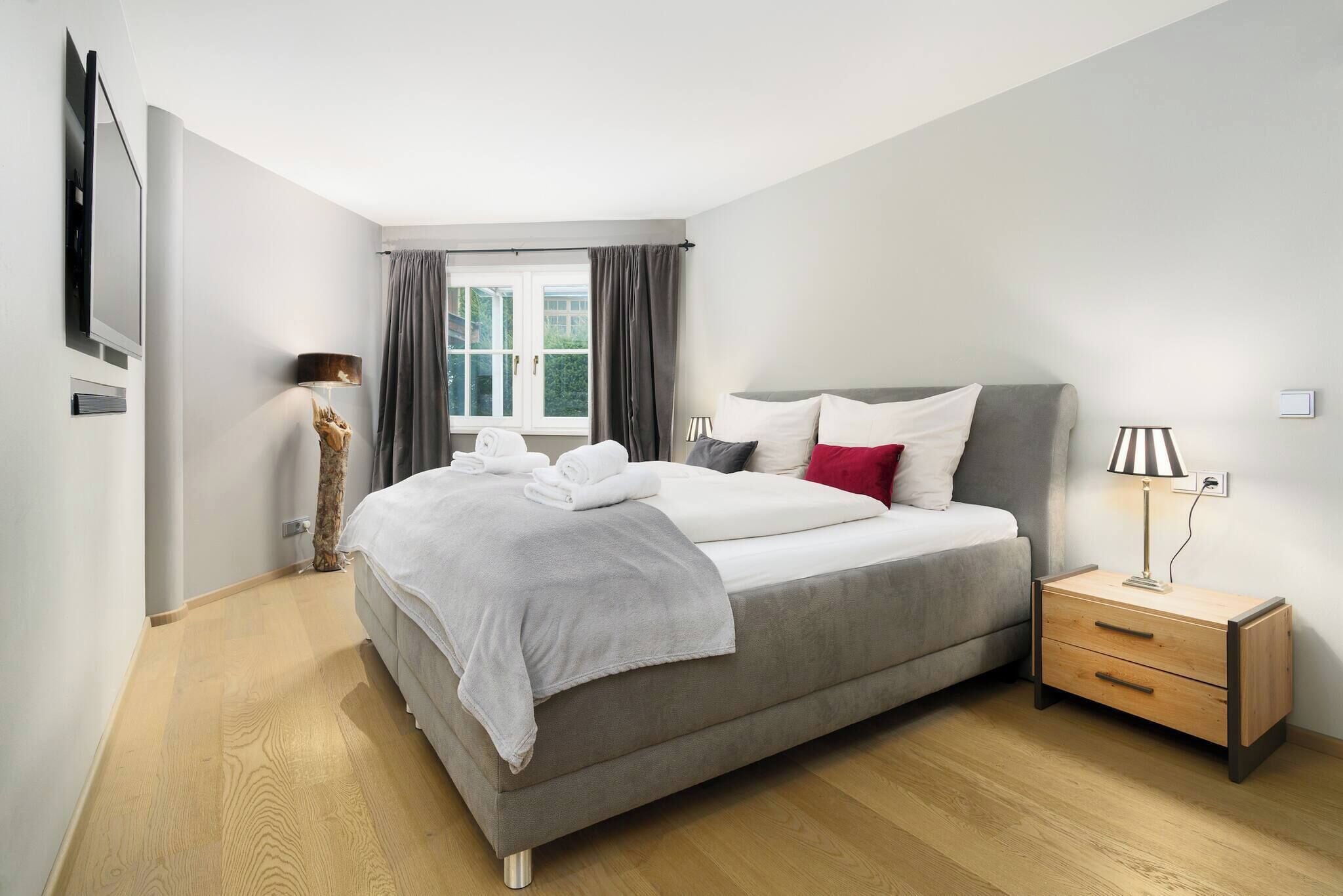 A modern bedroom with a large bed, bedside tables, a lamp, and a window with curtains.