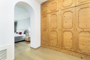 A bedroom with a grey sofa, a bedside table with a lamp, and a wooden wardrobe. - Kitz-Heart Premium Top 2 (Kitzbühel)