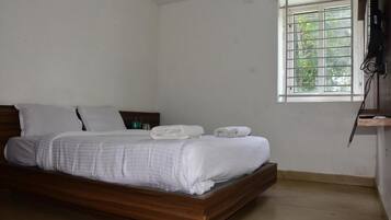 A single bed with white bedding, a wooden headboard, and a window with a view of greenery.