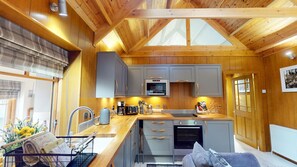 A compact kitchen with wooden beams, a built-in oven, and a window above the sink. - Wildcat Lodge - couples retreat for two with a hot tub (Boat of Garten)