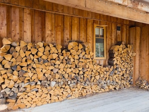 A stack of firewood against a wooden wall with a window. - Wildcat Lodge - couples retreat for two with a hot tub (Boat of Garten)
