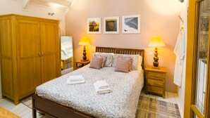 Un dormitorio con una cama grande, dos mesitas de noche con lámparas, un armario y tres cuadros en la pared.